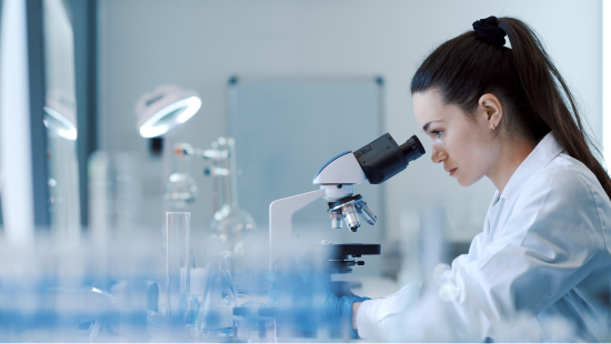 Person with ponytail looking down microscope in a lab